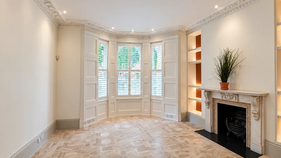 White bay-window shutters in a bright room with parquet flooring