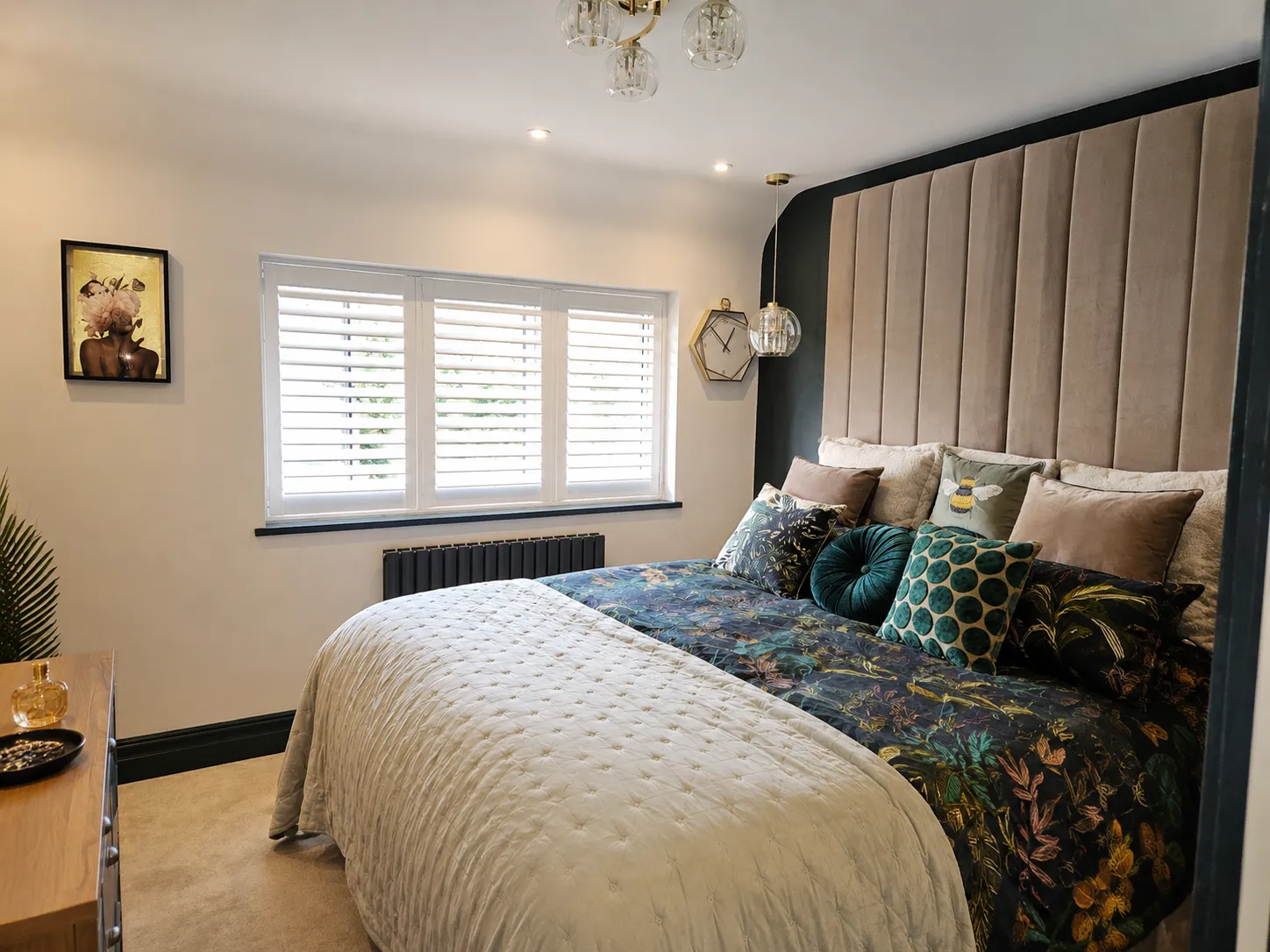 White full-height shutters beside a bed with a tall upholstered headboard