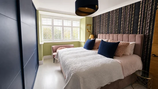 White bay-window shutters beside a bed with blue cushions