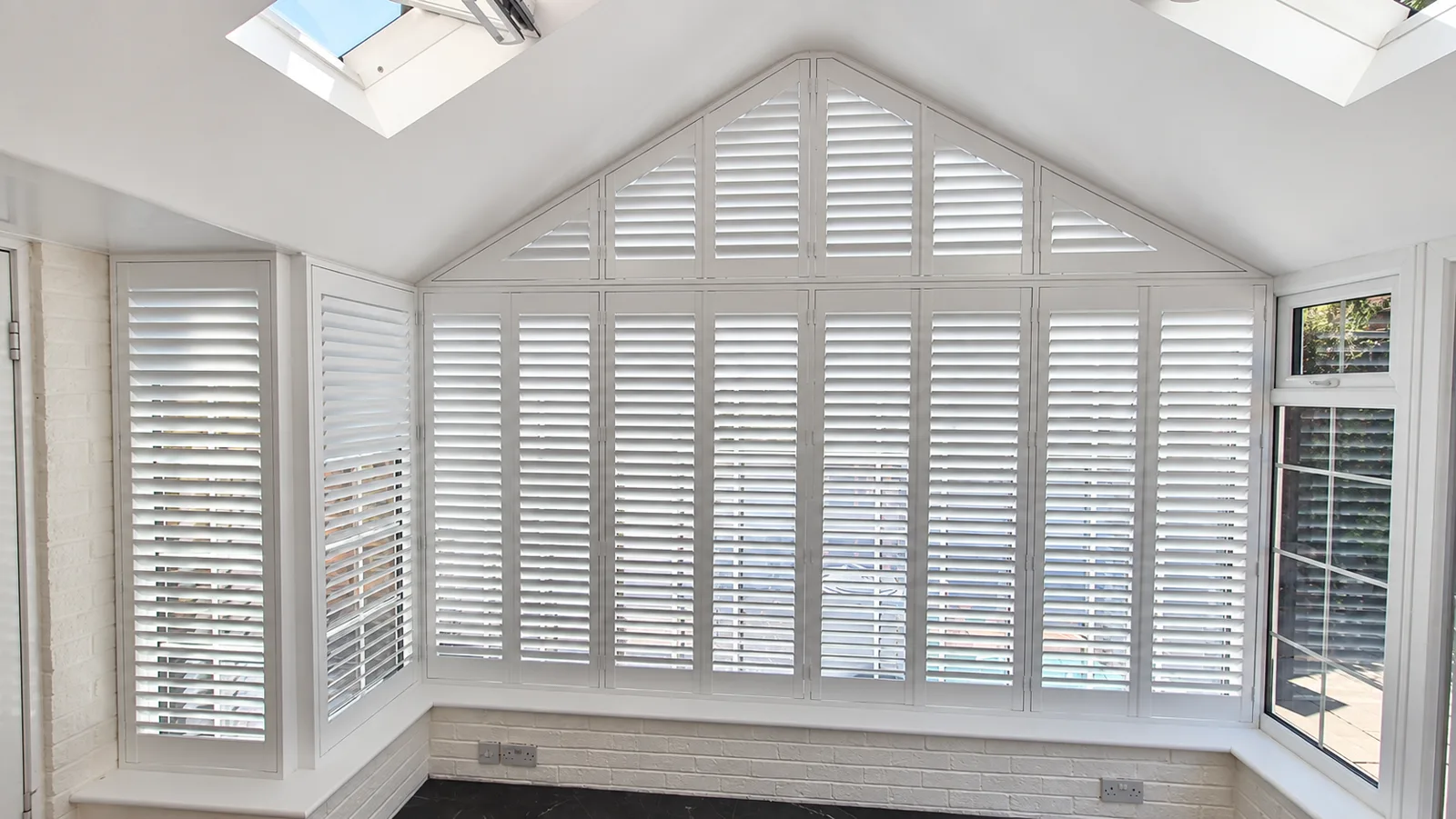 White shutters across the shaped windows of a pitched conservatory