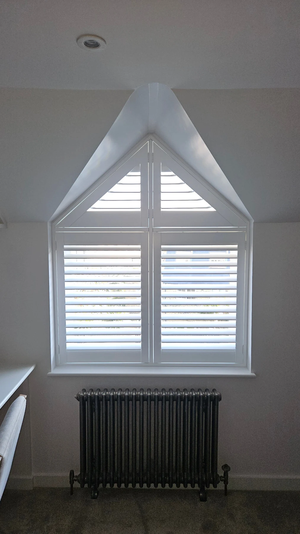 White shutters fitted to a pointed window beneath a sloping ceiling
